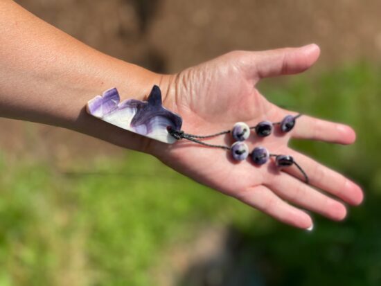 A photo of a hand holding a necklace with a whale-shaped pendant