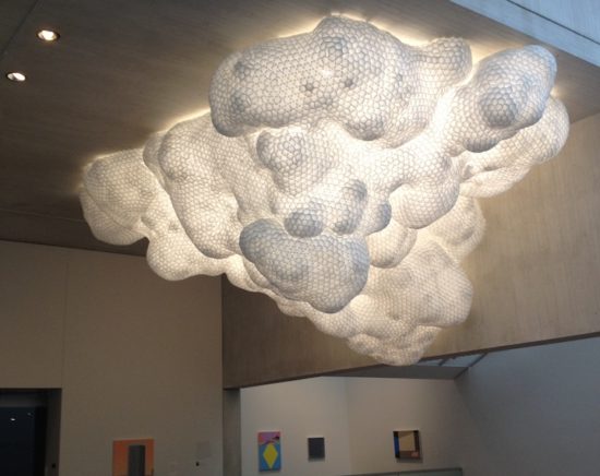 A photograph of “Untitled,” by Tara Donovan, a large, white amorphous sculpture mounted on the ceiling