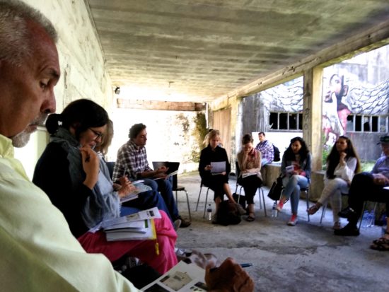 Photo of students encircles Pedro Soares Neves as they all read class material in an enclosed porch setting.