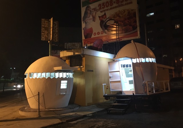 NuMu. Two white egg-shaped kiosks sit side-by-side on the street. One is strapped to a flatbed trailer, ready for transport.