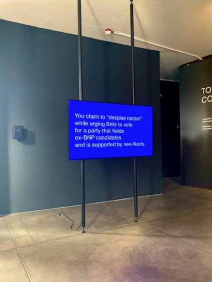 Tony Cokes's The Morrissey Problem, is an artwork shown on a flatscreen monitor suspended between 2 poles. The bright blue screen shows white text in a Serif font.