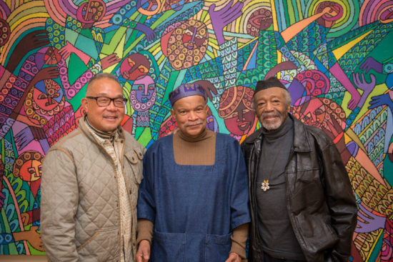 Three men stand in front of a colorful painting