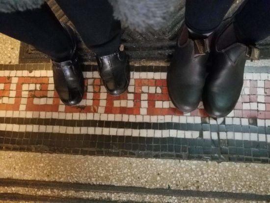 A photo of two pairs of black boots on a mosaic floor